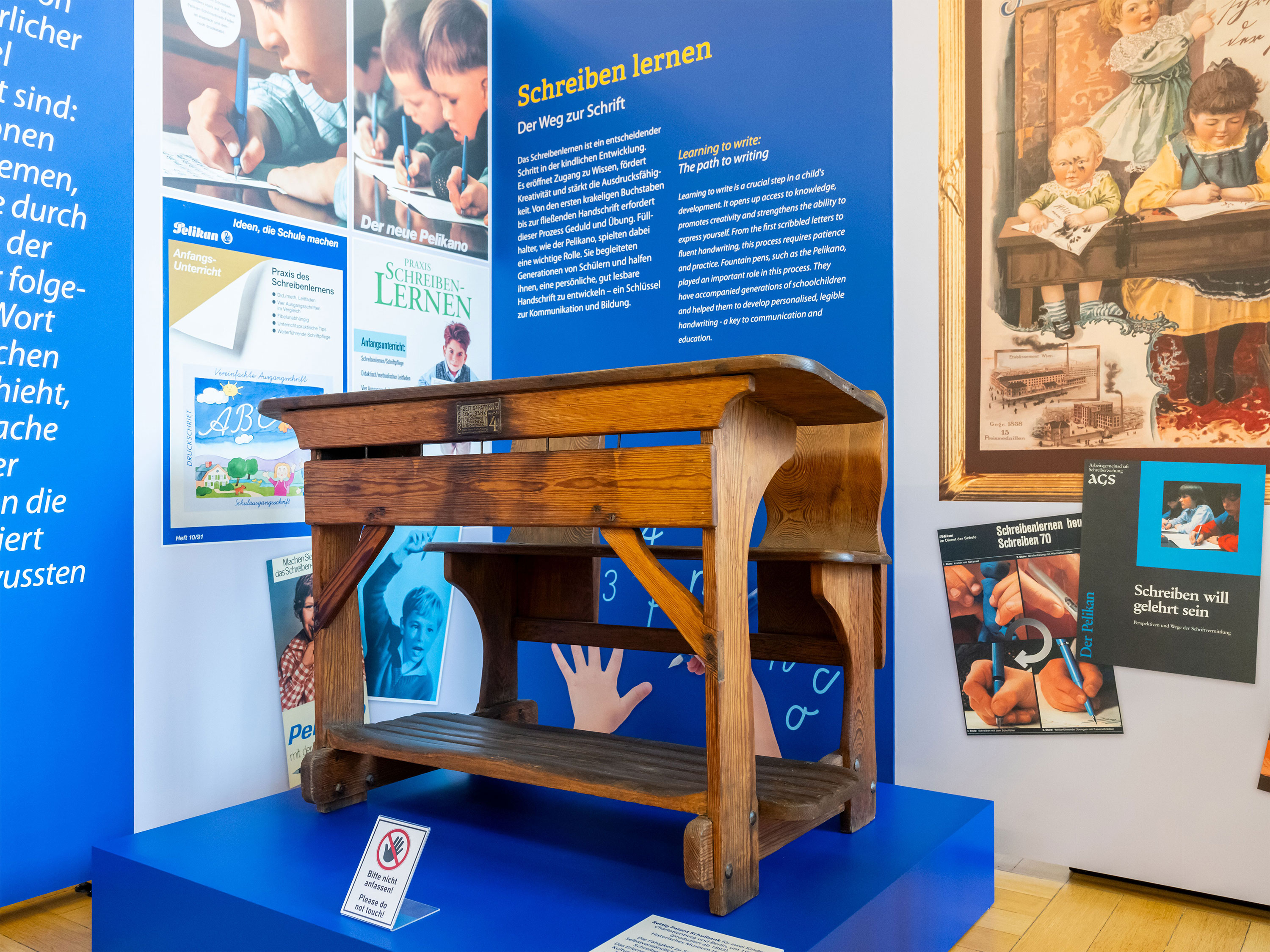 Alte Bank für Schüler in der Ausstellung, im Hintergrund Abbildungen und Texttafeln