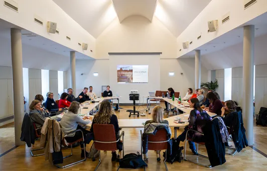 Workshop im Black History Month, 19 Frauen und Männer sitzen an U-förmig aufgestellten Tischen, im Hintergrund eine Präsentation auf einer Leinwand