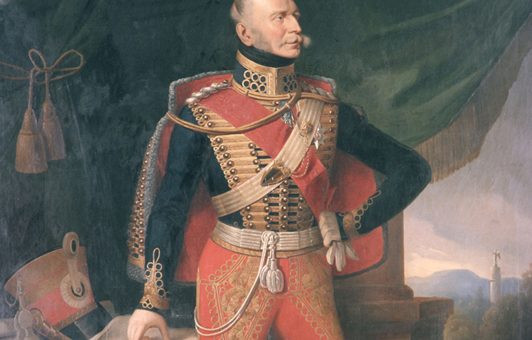König Ernst August von Hannover, Öl/Leinwand, Edmund Koken 1842; gemalt nach einem Bildnis von Franz Krüger, Gemäldeausschnitt. In der Bildmitte Ganzfigur des Königs in Husarenuniform (rote Hose, dunkelblauer, goldtressenbesetzter Rock, rot gefütterter Dolman) mit rotem Schulterband und Bruststern des St. Georgs-Ordens, den Kopf nach links gewandt, die linke behandschuhte Hand mit dem anderen Handschuh darin in die Hüfte gestemmt, hinter dem linken Bein der Schleppsäbel, rechte Hand auf eine Karte des Königsreichs Hannover weisend, die auf einem mit roter Decke behängten Tisch liegt; daneben der Tschako des Königs und eine Papierrolle